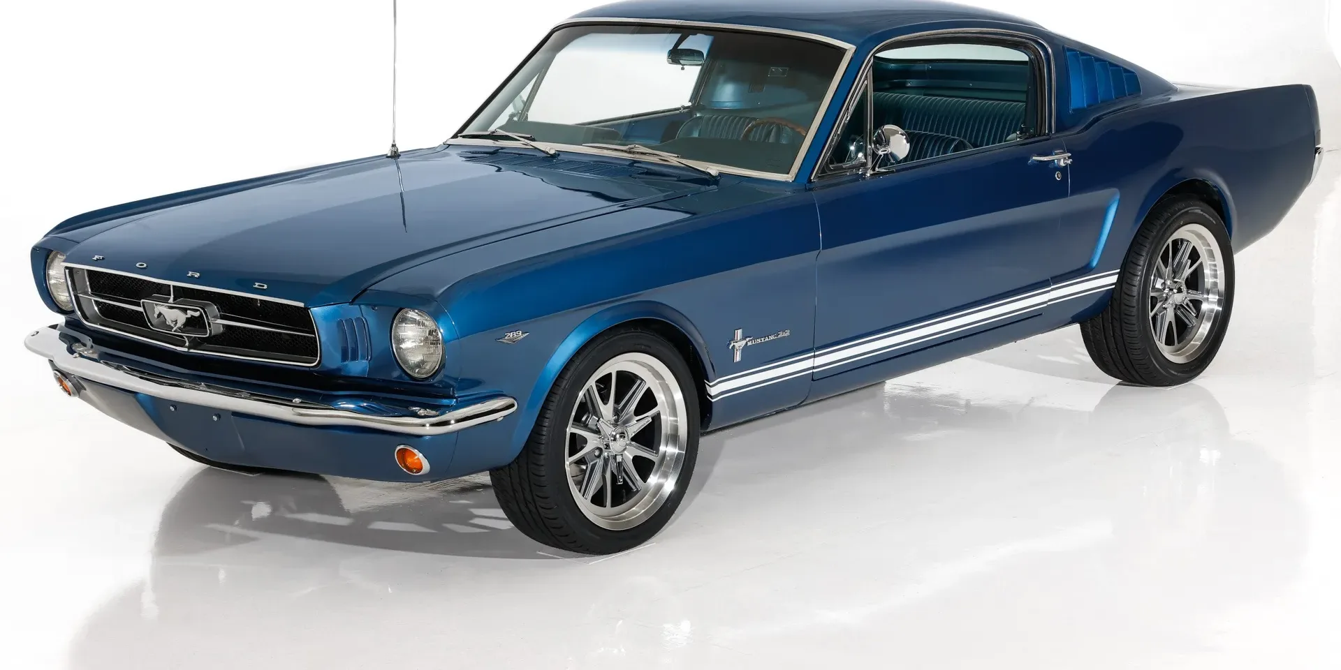 A blue 1965 Ford Mustang Fastback on a white studio floor
